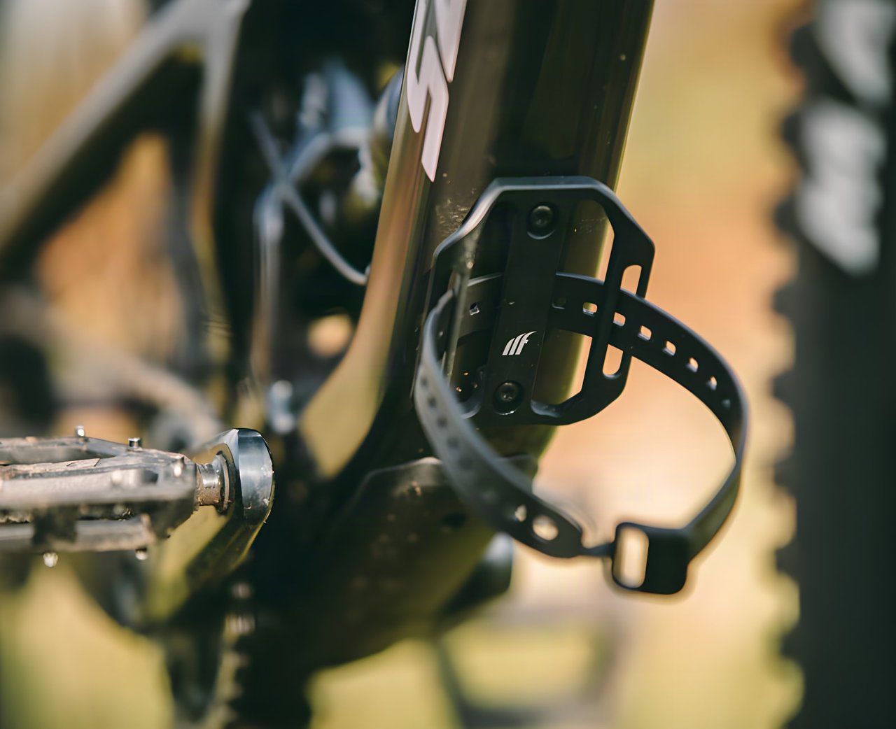 Black Tailfin Mini Cage with a strap, mounted on the down tube of a mountain bike above the crank.