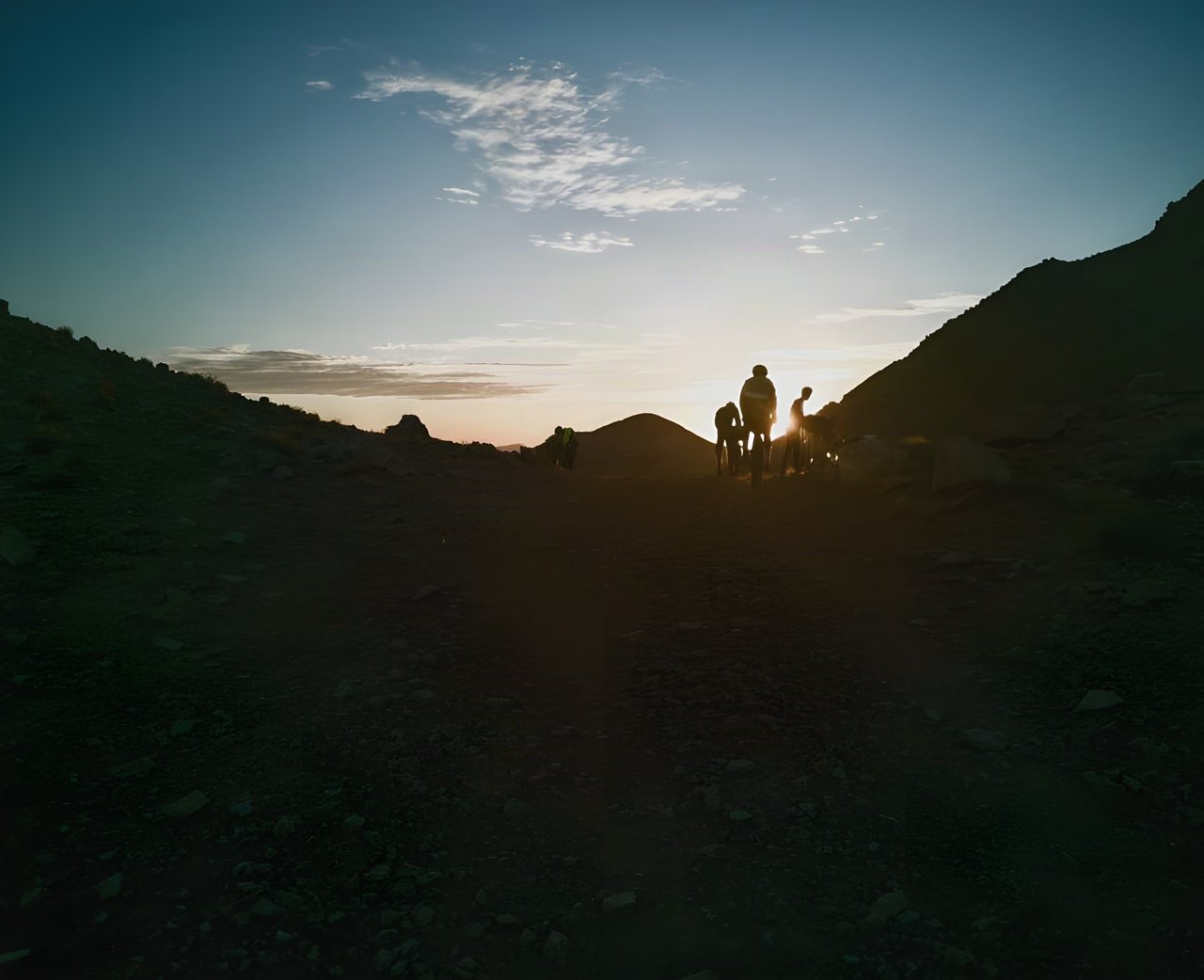 Atlas Mountain Race riders silhouetted against the low sun on a rocky mountain track in Morocco.