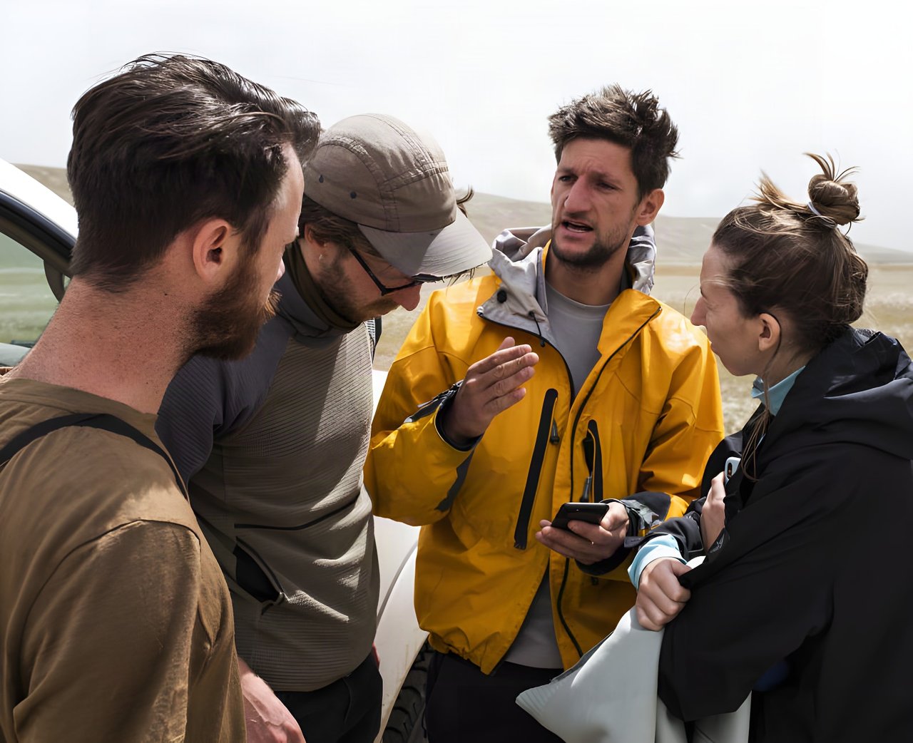 Four people confer over a phone beside a vehicle on open Kyrgyz steppe during the Silk Road Mountain Race.