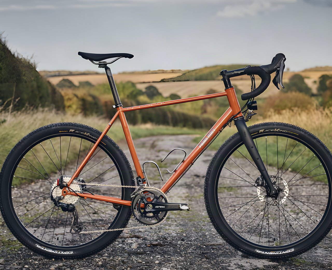 Fairlight Secan in orange with GRX cranks and Continental tyres, drive side, on a gravel track.
