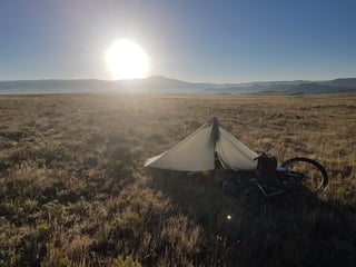 Tarp shelter and loaded bike pitched in dry grassland at sunrise near Salida, Colorado, on the Tour Divide.