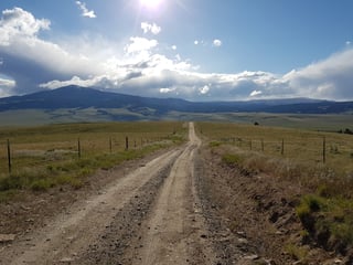 Gravel road runs straight across open Montana grassland towards distant mountains on the Tour Divide near Butte.