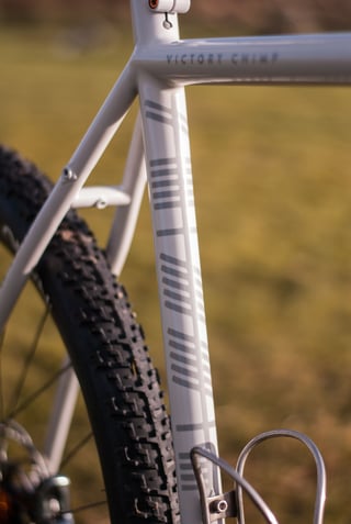 Seat tube of the Donard x Victory Chimp steel gravel bike, with grey Ogham markings above a stainless bottle cage.