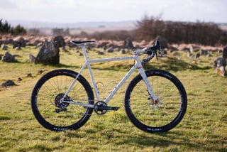 Side view of the Donard x Victory Chimp Gairbhéal bike with 27.5-inch wheels, parked among rocks in a field.