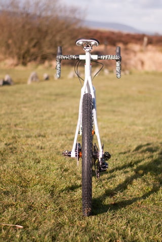Rear view of the Donard x Victory Chimp gravel bike on grass, with drop bars, a WTB tyre and rocks and moorland behind.