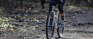 Rider on a Surly Midnight Special on a rough, leaf-strewn gravel track, cropped at the waist.