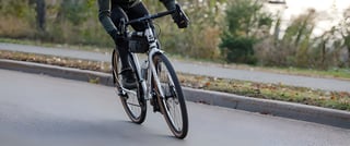 Rider on a Surly Midnight Special rolling along a tarmac road past a kerb and fallen leaves.
