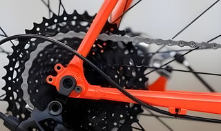 Gorilla Monsoon rear dropout, orange stay and thru-axle with the cassette and chain behind and a rear brake hose.