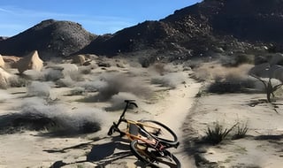 A Gorilla Monsoon lies on its side on a sandy desert trail below dark rocky hills.