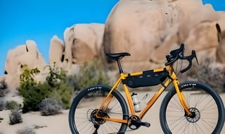 Gorilla Monsoon in orange and yellow with a frame bag and two bottles, parked in front of desert boulders.