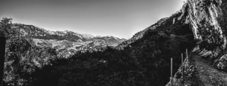 Monochrome view over a Mallorca valley from a rocky ledge trail with wooden fence posts.