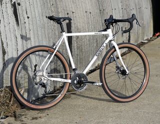 Surly Midnight Special in white on a concrete path beside a curved wall, drive-side three-quarter view.