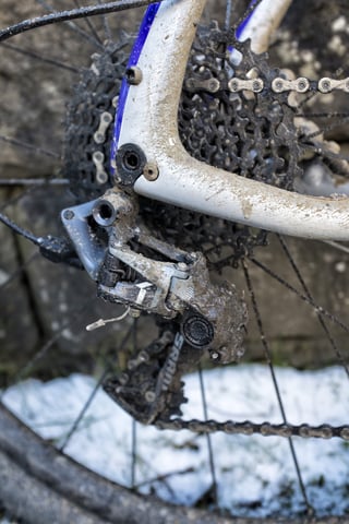 Muddy SRAM rear mech and cassette at the rear dropout of the Salsa Cutthroat, with snow on the ground below.