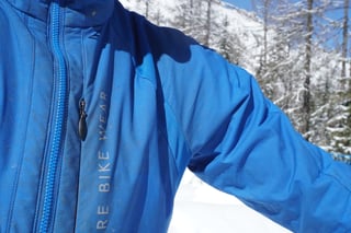 Chest zip and lettering detail on the Gore Wear Power Trail Primaloft jacket against a snowy Alpine backdrop.