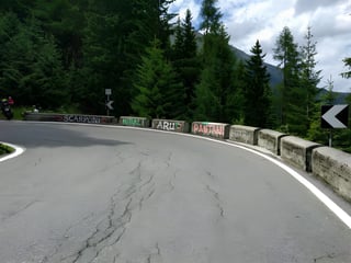 Hairpin bend on an Alpine climb with riders' names painted on the concrete barrier, including Scarponi and Pantani.