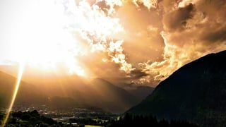 Low sun breaks through orange cloud over a mountain valley with a town below, in the evening on the Transalp.