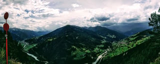 Panorama of a wide Alpine valley with a river and villages beneath dark cloud, from the Gacher Blick viewpoint.