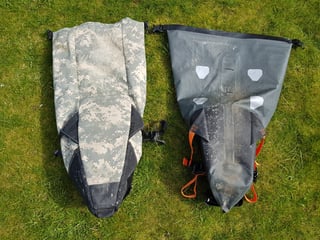Camouflage Revelate Viscacha and grey Ortlieb seat pack laid side by side on grass to compare their shape.