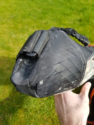 Hand holding the worn, creased tapered end of a Revelate Viscacha seat pack that has deformed with use.