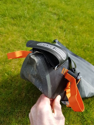 Hand holding the reinforced tapered end of the Ortlieb seat pack, with its waterproof label and orange strap.