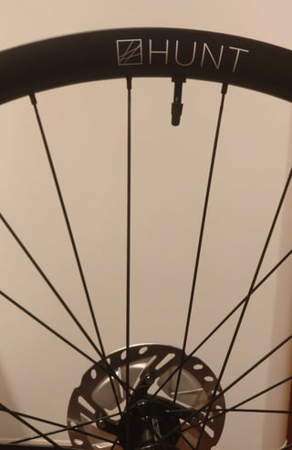 Hunt logo on the carbon rim of the 30 Carbon Gravel wheel, with valve stem and spokes above the disc rotor.