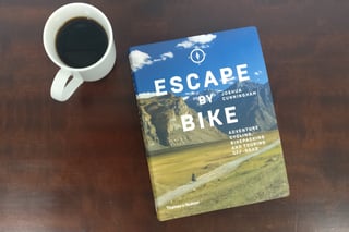 Front cover of Escape By Bike by Joshua Cunningham, published by Thames &amp; Hudson, beside a cup of black coffee.