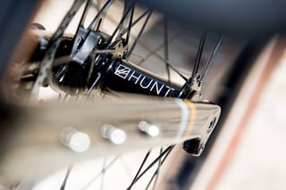 Close-up of the black Hunt front hub and fork dropout on the Bombtrack Audax, spokes blurred.