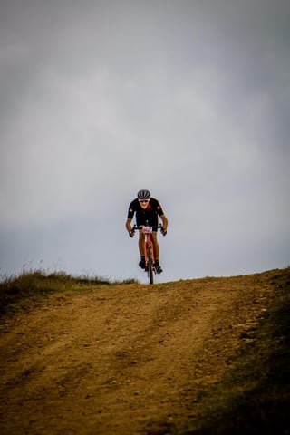 Lone Yorkshire True Grit rider on an orange gravel bike crests a dirt track beneath a heavy grey sky.