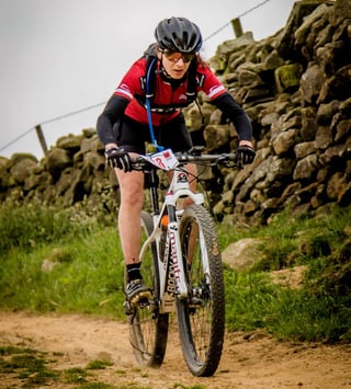 Rider on a white full-suspension mountain bike takes a stony track beside a dry stone wall at Yorkshire True Grit.