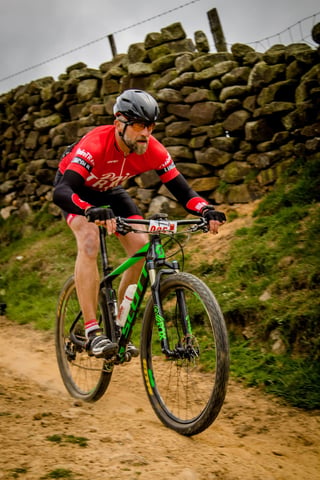 Rider in a red jersey on a green Scott mountain bike passes a dry stone wall at Yorkshire True Grit.