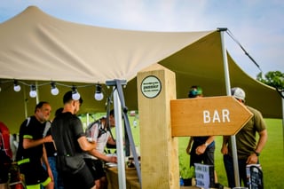 Wooden signpost pointing to the bar beneath a canvas tent at The Distance overnight camp.
