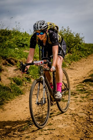 Smiling rider in pink socks takes a gravel bike along a rutted dirt track at Yorkshire True Grit 2018.