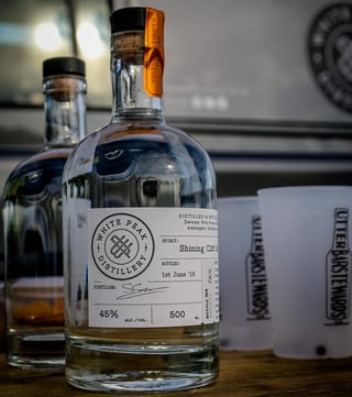 Bottle of White Peak Distillery Shining Cliff gin beside plastic cups at The Distance camp.