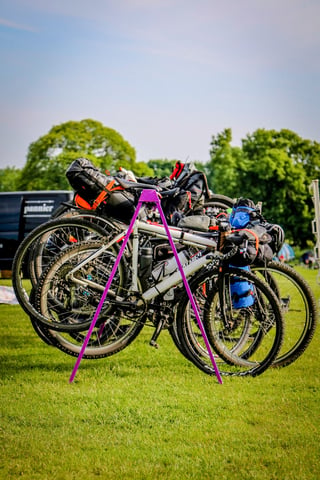 Bikepacking bikes with bags lean on a purple stand in front of a Pannier van at The Distance camp.
