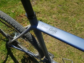 Close-up of the True Grit logo on the top tube of the Lauf True Grit carbon frame, with a gravel tyre behind.