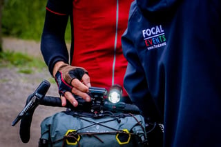 Close-up of an Apidura handlebar bag, front light and SRAM lever beside a Focal Events organiser on The Distance.