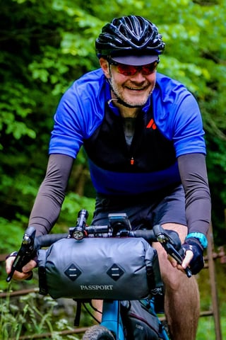 Grinning rider in a blue jersey with a Passport handlebar bag and Shimano levers on The Distance.