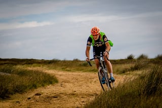 Rider in an orange helmet with a green pack rides a gravel bike along a moorland track at Yorkshire True Grit.