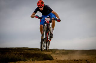 Rider in an orange helmet jumps a mountain bike over a moorland crest at Yorkshire True Grit.