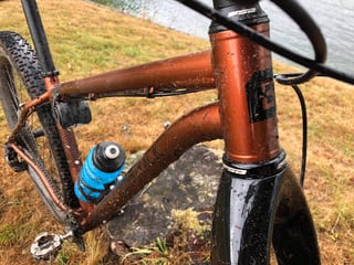 Muddy copper head tube, top tube and down tube of the Bombtrack Beyond+ 2 with a blue bottle in the cage.