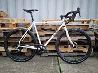 White Surly Midnight Special gravel bike in Ison's UK spec, shown side-on against stacked wooden pallets.