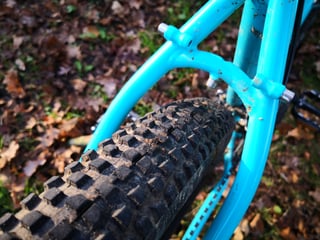 Close-up of the Surly Bridge Club seat stays arching over a muddy knobbly tyre, with braze-on bolts.