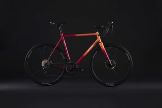 All-City Zig Zag disc road bike in the orange-red fade, side view against a dark studio backdrop.