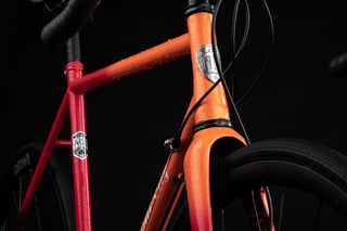 Head tube badge and A.C. seat tube decal on the orange-red fade All-City Zig Zag frame, front tyre beyond.
