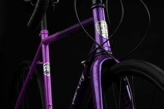 Head tube badge and steel tubing of a purple All-City Zig Zag, seen from low down in the studio.