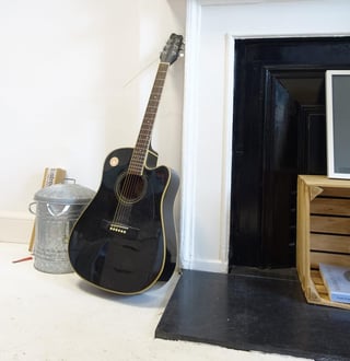 Acoustic guitar leaning against the wall beside a fireplace in the Straight Cut studio in Edinburgh.