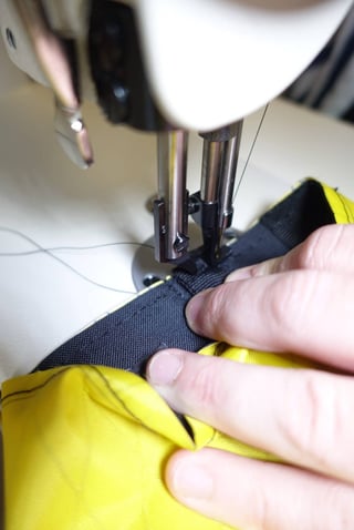 Close-up of a sewing machine stitching black fabric onto the yellow lining of a Straight Cut bag.