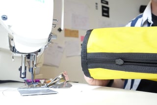 Yellow X-Pac bar bag with a black zip held beside a Juki sewing machine in the Straight Cut studio.