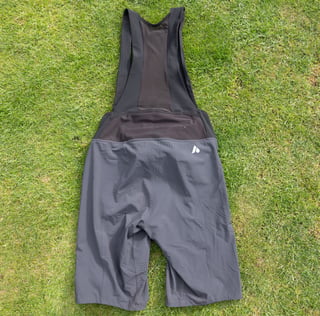 Rear view of the Aussie Grit Apparel Ignite 2-in-1 bib shorts laid flat on grass, with mesh straps and vent holes.