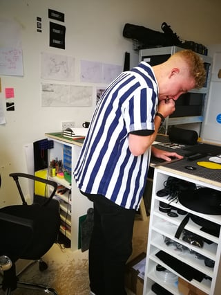 Ross O'Reilly leans over his workbench in the Straight Cut studio planning a bag, with design sketches on the wall.